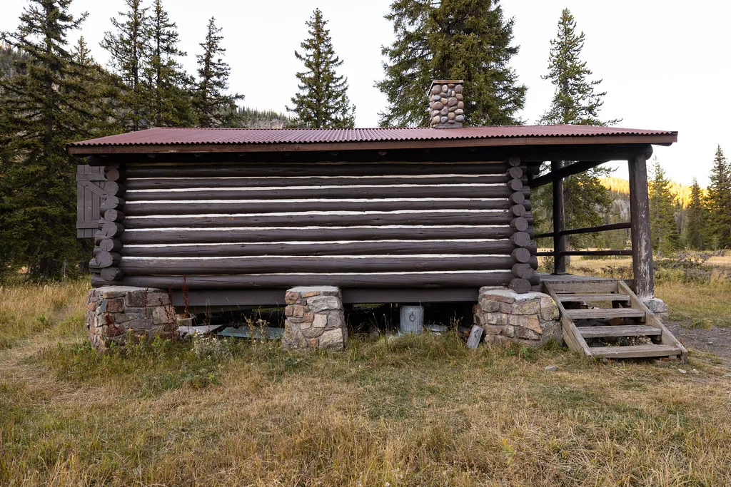 Long log cabin with a side porch on a grassy slope