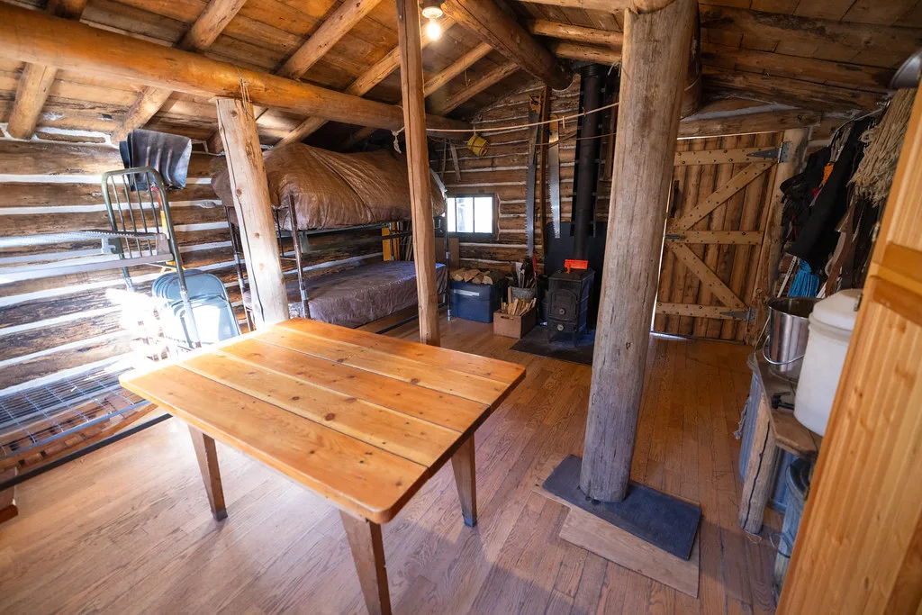Sleeping area with bunks and a wood stove beside timber posts and a plank table