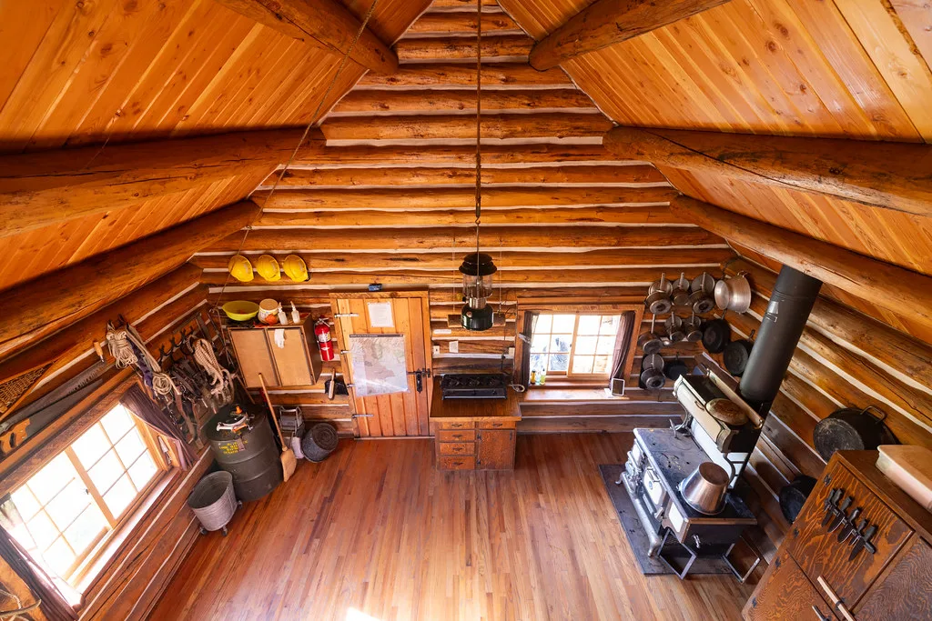Log cabin interior viewed from the loft, with a cookstove and plank floor