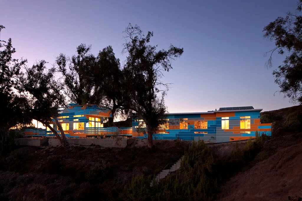 House glowing at dusk on a hillside beneath trees