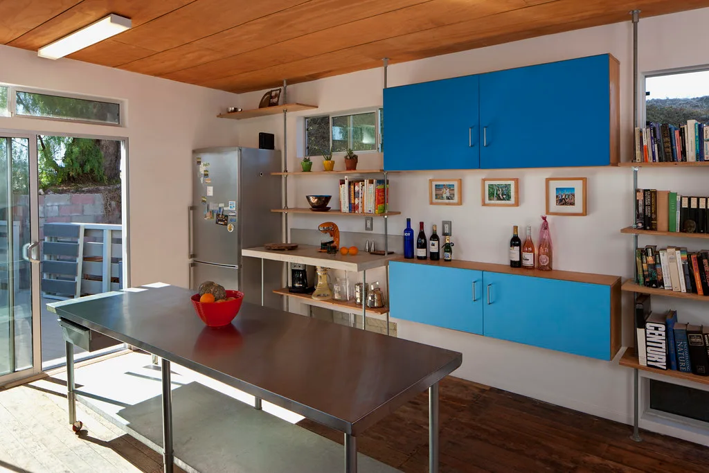 Steel kitchen table beside built-in blue cabinets and open shelves