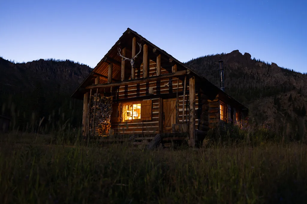 Log cabin with a lit window at dusk