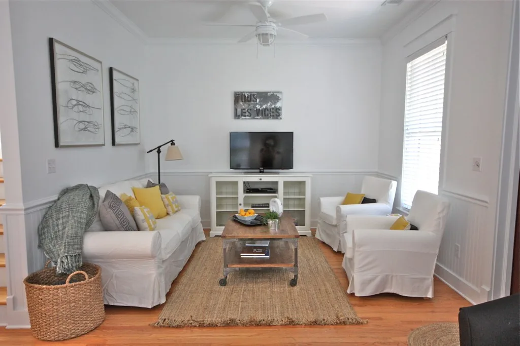White living room with slipcovered sofa and armchairs, yellow cushions and a TV on a white console