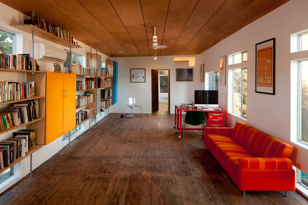 Long living room lined with bookshelves, an orange sofa and recycled wood floors