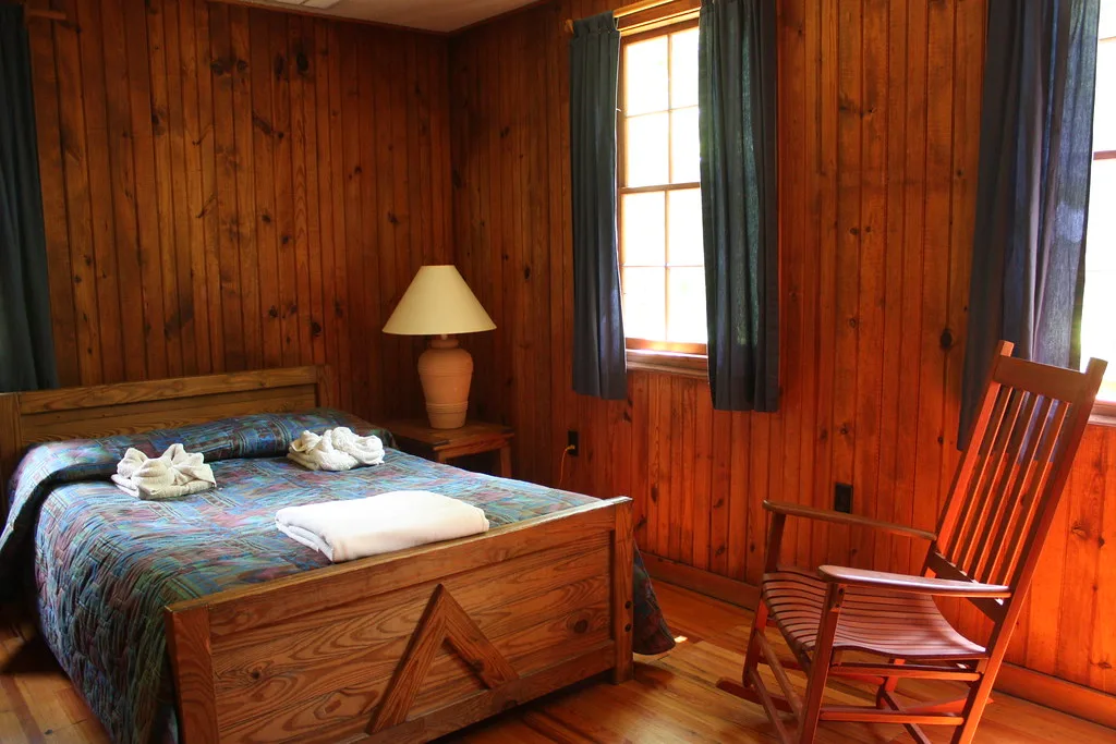 Pine-panelled bedroom with a quilted bed, lamp and rocking chair