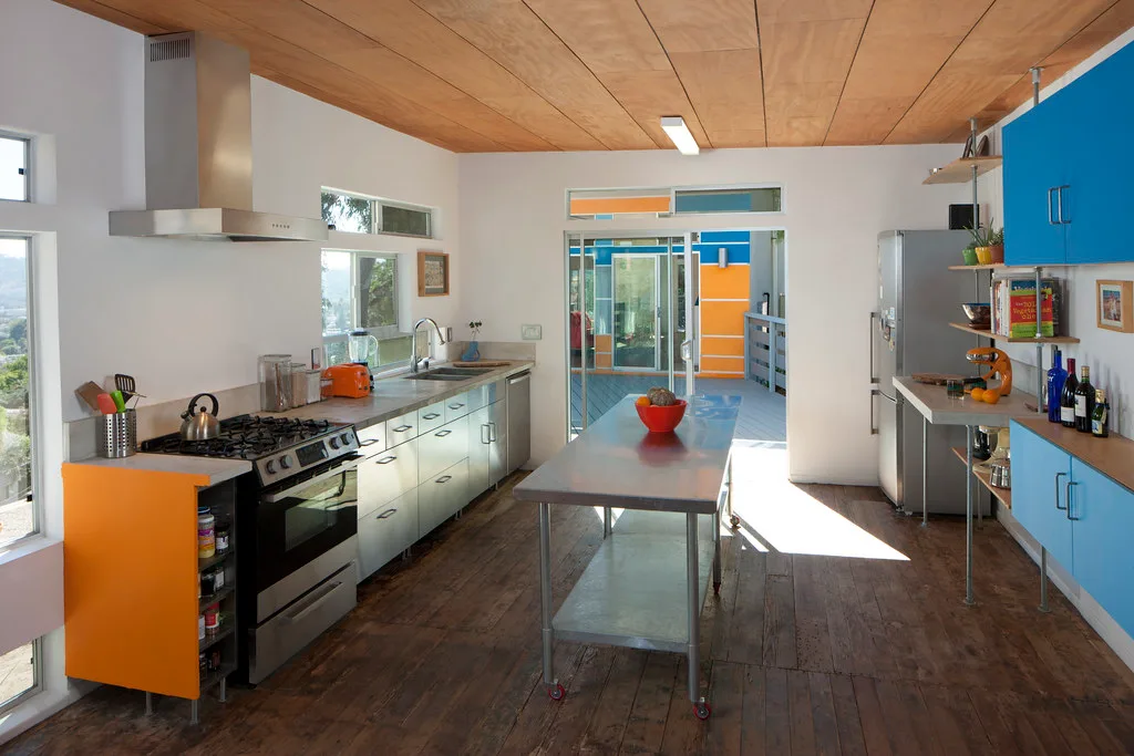 Kitchen with orange and blue cabinets, steel island and plywood ceiling